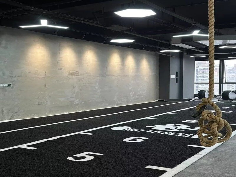 Spacious gym with green padded turf flooring for a functional training zone, featuring a black sled and battle ropes.